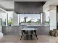 Cucina moderna con isola centrale in acciaio opaco, piano in marmo, tavolo e sedie. Ampia finestra con vista sul verde.