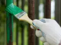 Mano guantata che vernicia di verde un palo di metallo arrugginito, rinnovando la verniciatura.