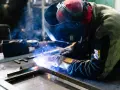 Saldatore al lavoro, scintille luminose e fumo blu avvolgono la tempra dell'acciaio inox.