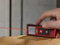 Dito come si usa il metro laser Milwaukee per misurazioni precise. Un dito preme il pulsante per attivare il raggio laser rosso.
