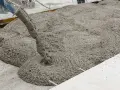 Il cemento fresco viene versato da una betoniera, mostrando come si fa il cemento per una nuova pavimentazione.