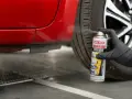 Mano con guanto nero spruzza spray "Deca Flash" su un'auto rossa per come sciogliere la colla secca e residui adesivi.