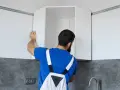 Installazione di pensili da cucina: un uomo con tuta blu monta un pensile angolare su una guida a muro.