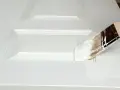 Pennello bianco applica vernice su porta in legno già verniciata, mostrando come verniciare una porta in legno già verniciata.