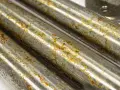 Tre tubi metallici mostrano segni di ruggine e corrosione, con l'acciaio annerisce in alcune aree.