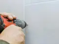 Mani che usano un trapano per fare un buco nel muro bianco.