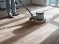 Un professionista usa una levigatrice per decerare il parquet, sollevando una nuvola di polvere.