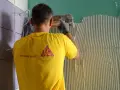 Un operaio con maglia gialla applica colla sul muro, mostrando come attaccare piastrelle.