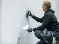 Operaio con cazzuola lavora su un muro esterno, mostrando come rasare un muro rovinato per un aspetto liscio e uniforme.