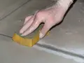 Mano con guanto in lattice che rifinisce le fughe dei pavimenti con una spugna umida.