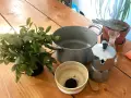 Preparativi per come invecchiare il legno con il caffè: moka, pentola, ciotola con fondi di caffè, pianta e un vaporizzatore.