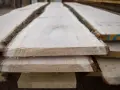 Tavole di legno grezzo impilate, con la corteccia ancora presente, pronte per il processo di stagionatura che ne assicura la durabilità.