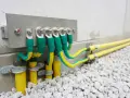 Cavi verdi e gialli collegati a una barra di messa a terra su una parete di cemento, con tubi gialli che escono dal terreno.