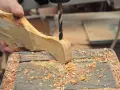 Mano che trapana un pezzo di legno grezzo, creando un tagliere legno fai da te. Segatura ovunque.
