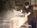 Falegname usa pialla elettrica su un grosso tronco di legno, creando una nuvola di segatura. Il piallare significato è dare una finitura liscia.