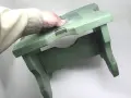 Mano che tiene uno sgabello di legno verde, pronto per verniciare con bomboletta spray.