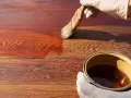 Mano guantata applica una vernice scura su assi di legno, mostrando come scurire il legno per un aspetto più profondo e ricco.