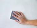 Mano che leviga una parete con carta vetrata, mostrando le sue caratteristiche abrasive per una finitura liscia.