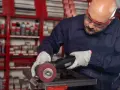 Operaio con occhiali protettivi e guanti lavora su un pezzo metallico, usando una smerigliatrice. Impara come saldare acciaio inox con precisione.