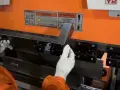 Mani guantate posizionano un pezzo di metallo per piegare ferro fai da te su una pressa piegatrice.