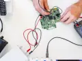 Mani che usano un multimetro per regolare uno strumento di misura su una scheda elettronica.