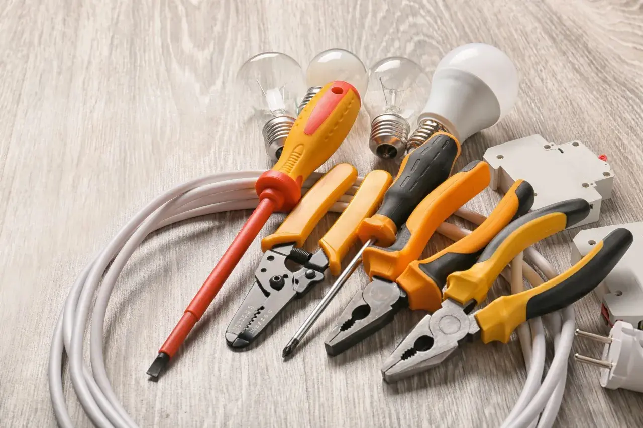 Un set di strumenti per elettricisti: pinze, cacciaviti, lampadine e cavi su un tavolo di legno.