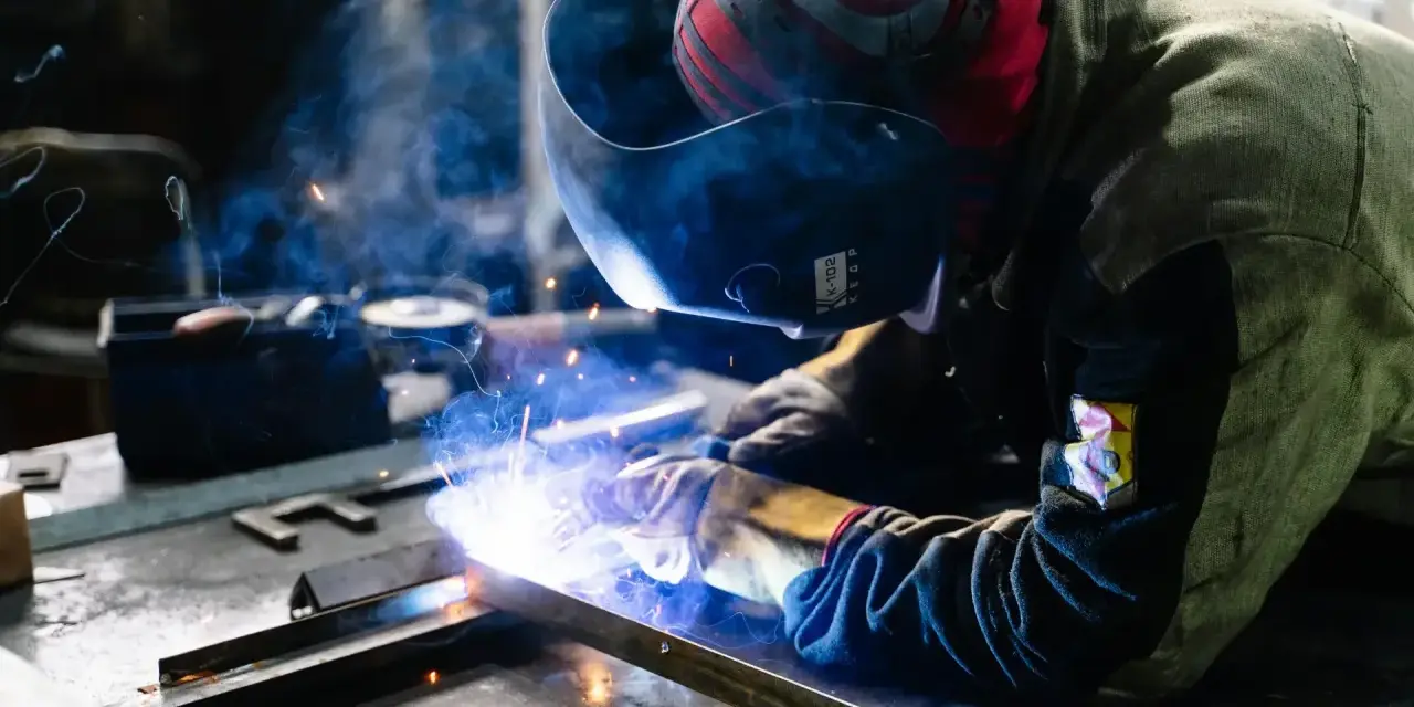 Saldatore al lavoro, scintille luminose e fumo blu avvolgono la tempra dell'acciaio inox.