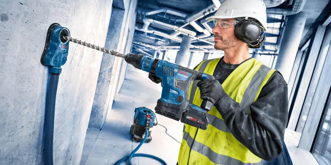 Operaio con trapano a percussione e punte trapano per cemento armato, pronto a forare un muro in cantiere.