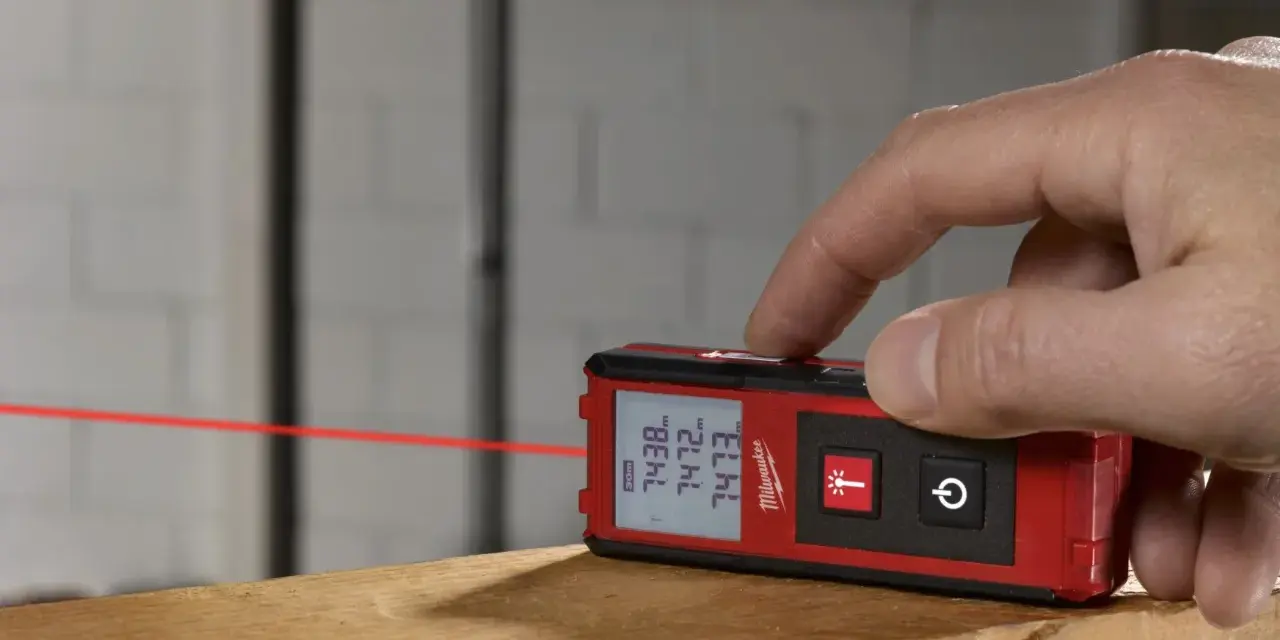 Dito come si usa il metro laser Milwaukee per misurazioni precise. Un dito preme il pulsante per attivare il raggio laser rosso.
