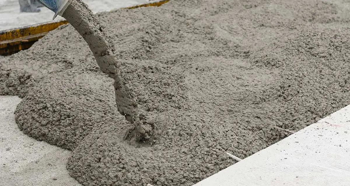 Il cemento fresco viene versato da una betoniera, mostrando come si fa il cemento per una nuova pavimentazione.