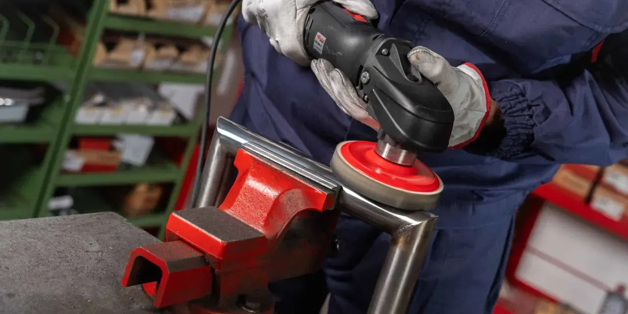 Operaio usa una lucidatrice con dischi abrasivi, parte dei prodotti per lucidare l'acciaio, per rifinire un pezzo metallico fissato in una morsa.