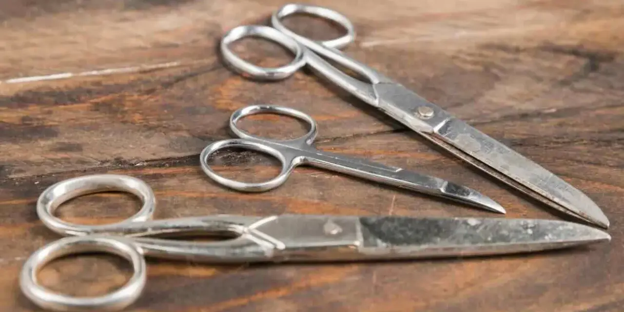 Tre forbici di metallo su un tavolo di legno. Scopri come togliere la ruggine dalle forbici per farle tornare come nuove.