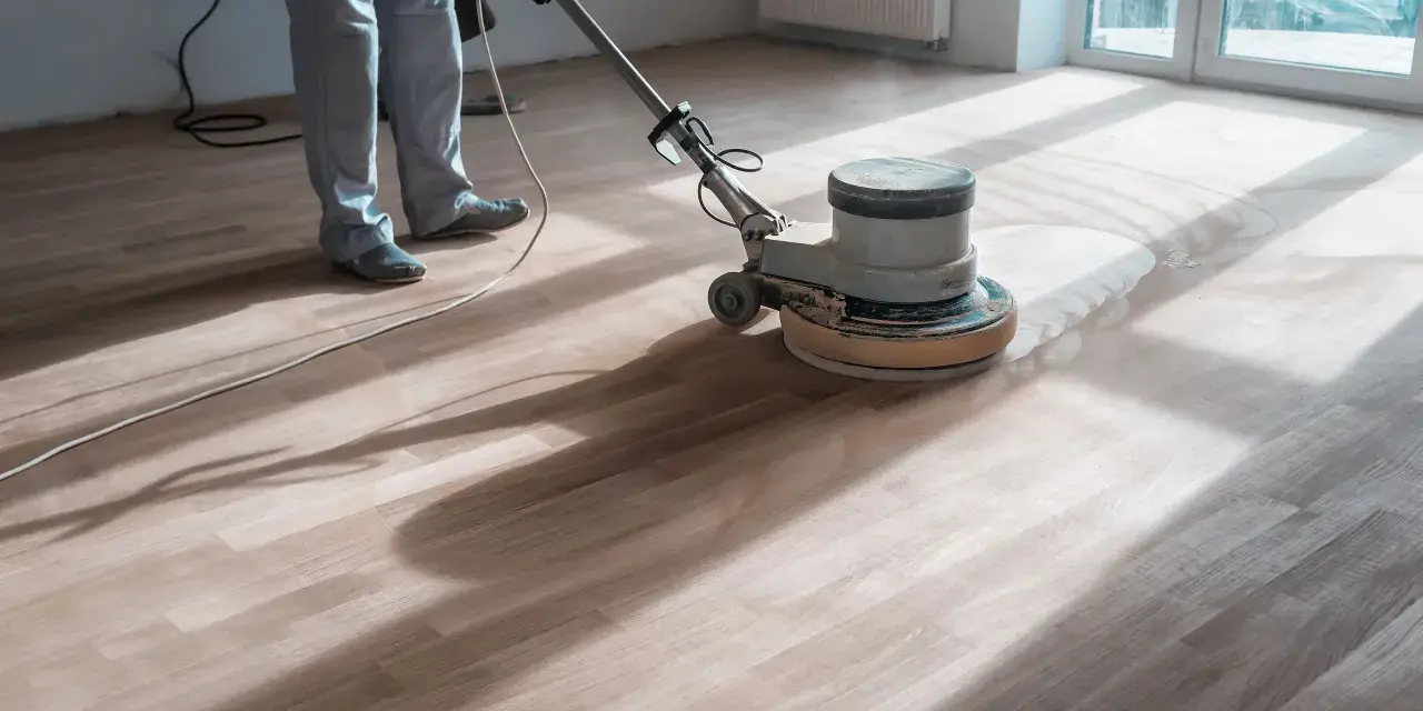 Un professionista usa una levigatrice per decerare il parquet, sollevando una nuvola di polvere.