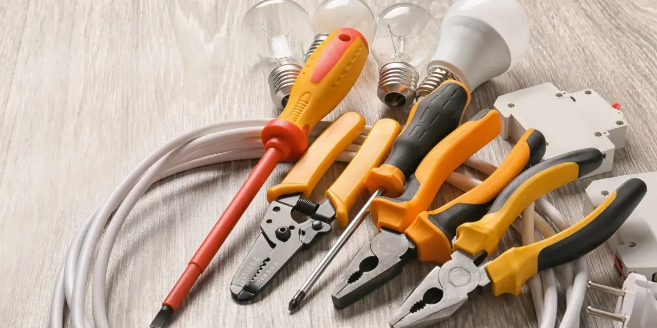 Un set di strumenti per elettricisti: pinze, cacciaviti, lampadine e cavi su un tavolo di legno.
