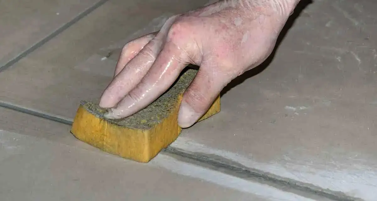 Mano con guanto in lattice che rifinisce le fughe dei pavimenti con una spugna umida.