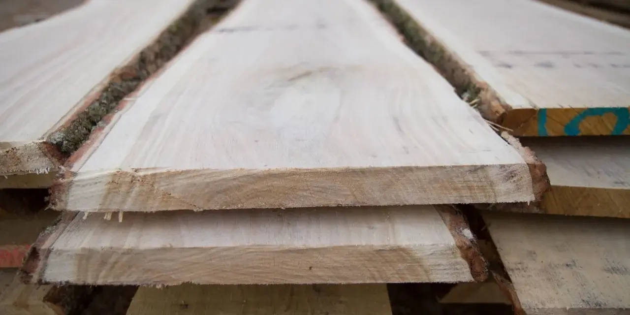 Tavole di legno grezzo impilate, con la corteccia ancora presente, pronte per il processo di stagionatura che ne assicura la durabilità.