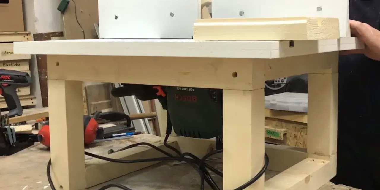 Banco fresa fai da te con fresatrice Bosch montata sotto il piano di lavoro. Un pezzo di legno viene lavorato.