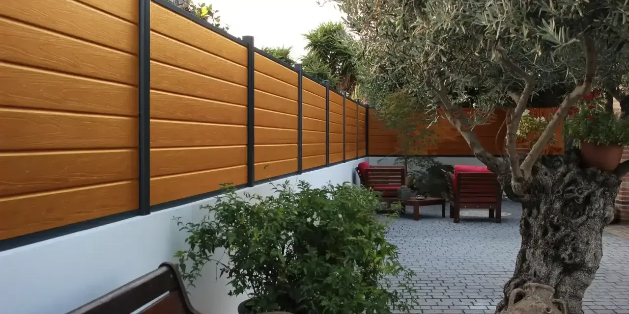 Pannello in legno effetto teak fissato a un muro bianco, con un ulivo secolare e arredi da esterno. Ideale per capire come fissare un pannello di legno al muro.