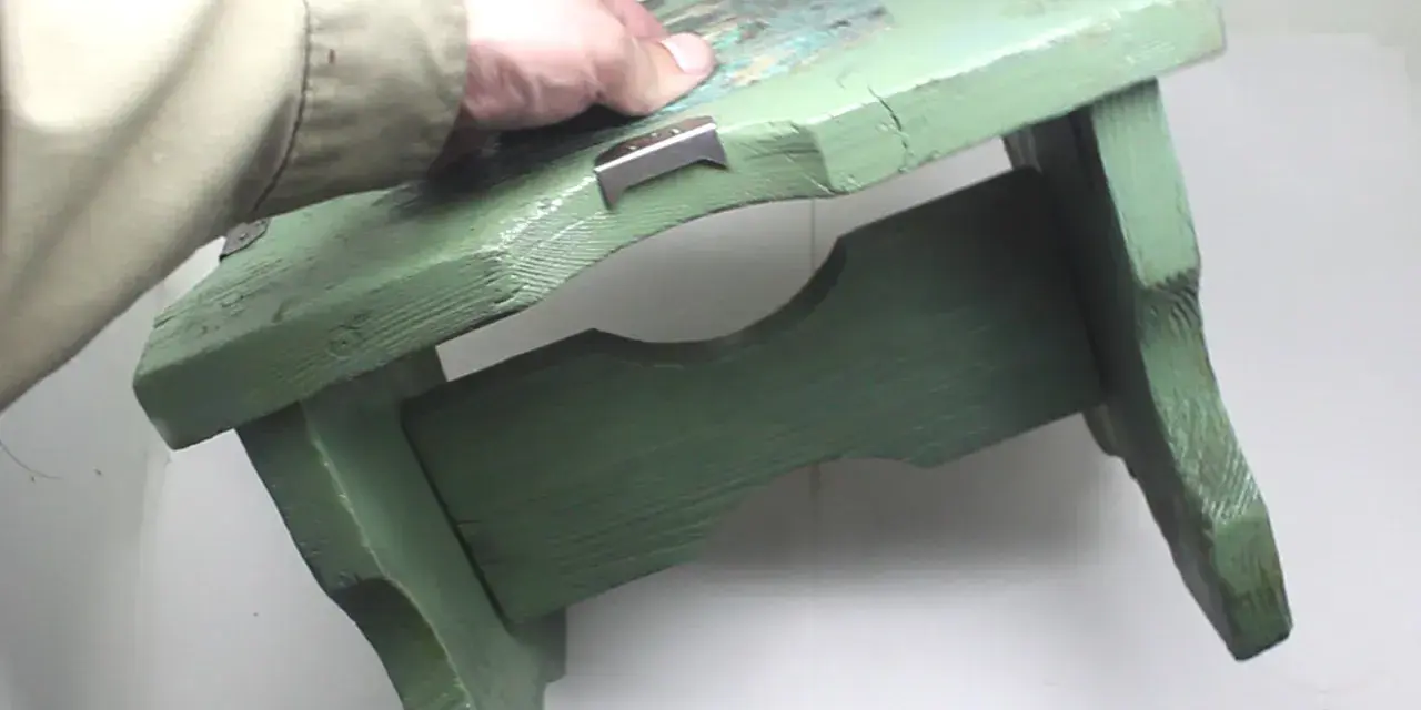 Mano che tiene uno sgabello di legno verde, pronto per verniciare con bomboletta spray.