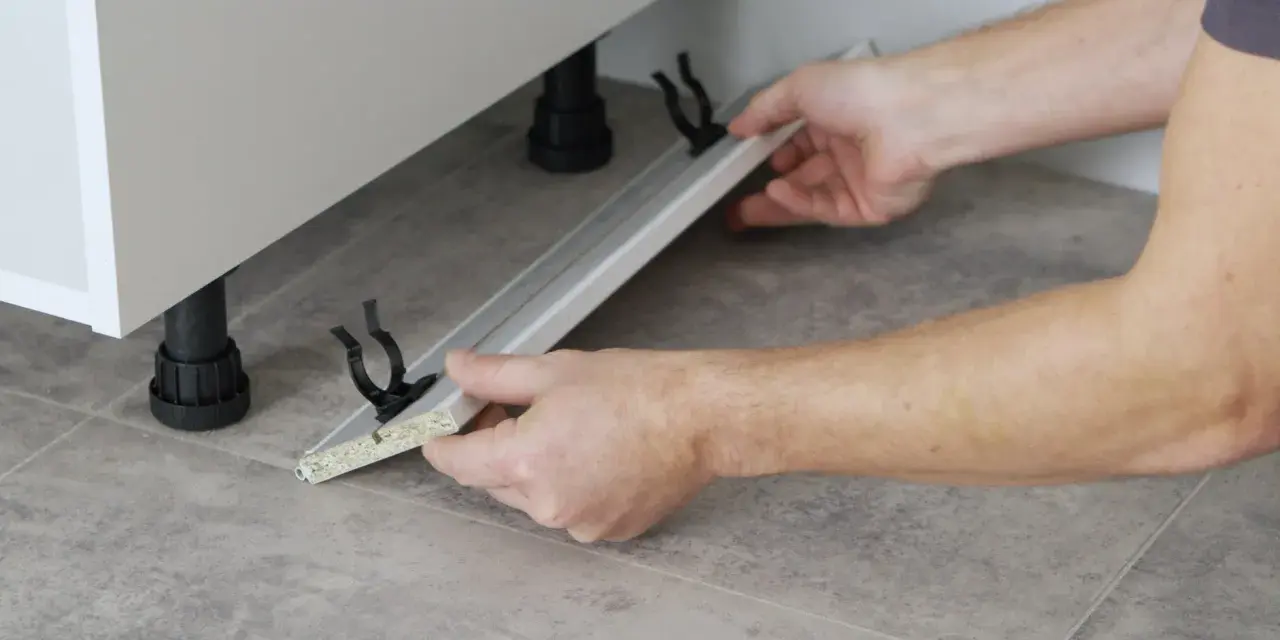 Mani che assemblano uno zoccolo cucina in alluminio, mostrando come tagliare e fissare i supporti.
