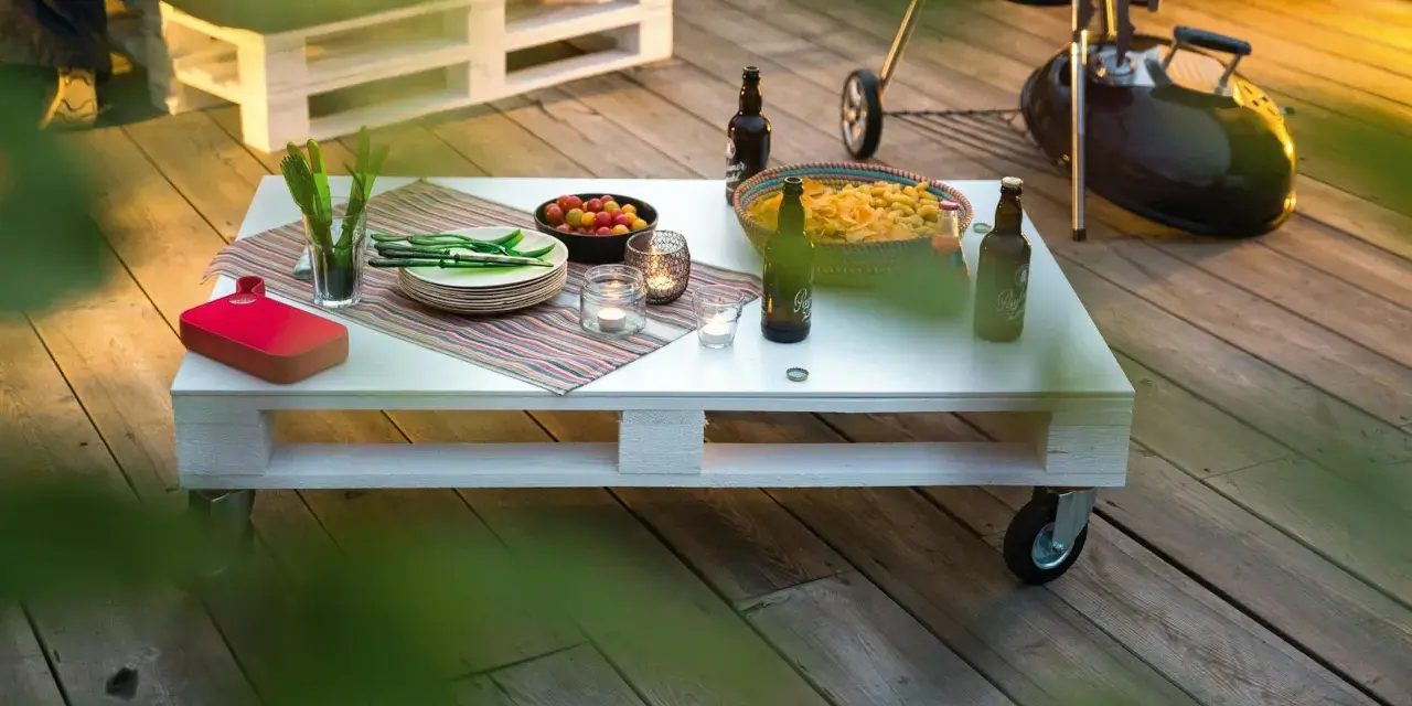 Tavolo con pallet fai da te, pronto per un barbecue con birre, patatine e pomodorini.