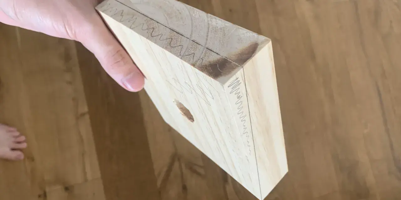 Mano che tiene un pezzo di legno con segni di matita, come se si stesse pensando a come tagliare il legno senza attrezzi.