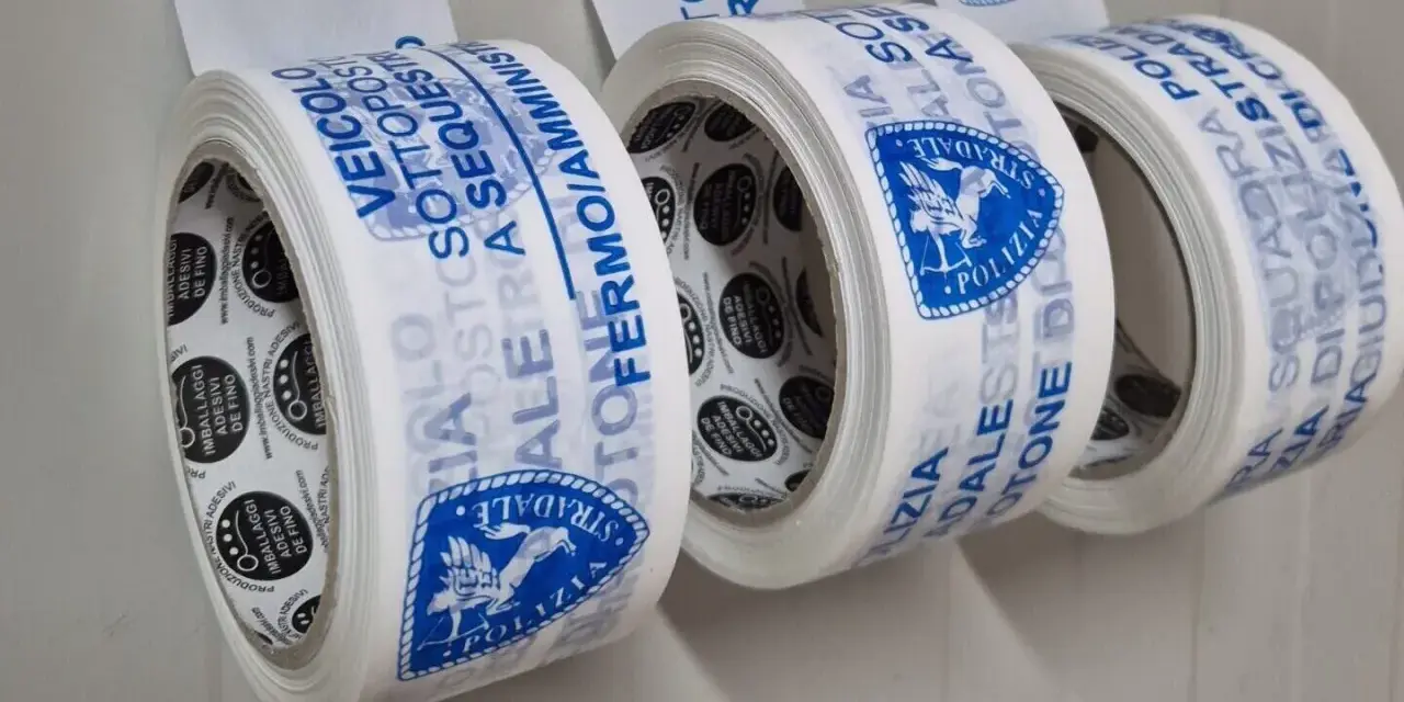 Rotoli di nastri adesivi con scritte blu: "Veicolo Sottosequestro", "Polizia Stradale". Diversi tipi di nastri per imballaggi.