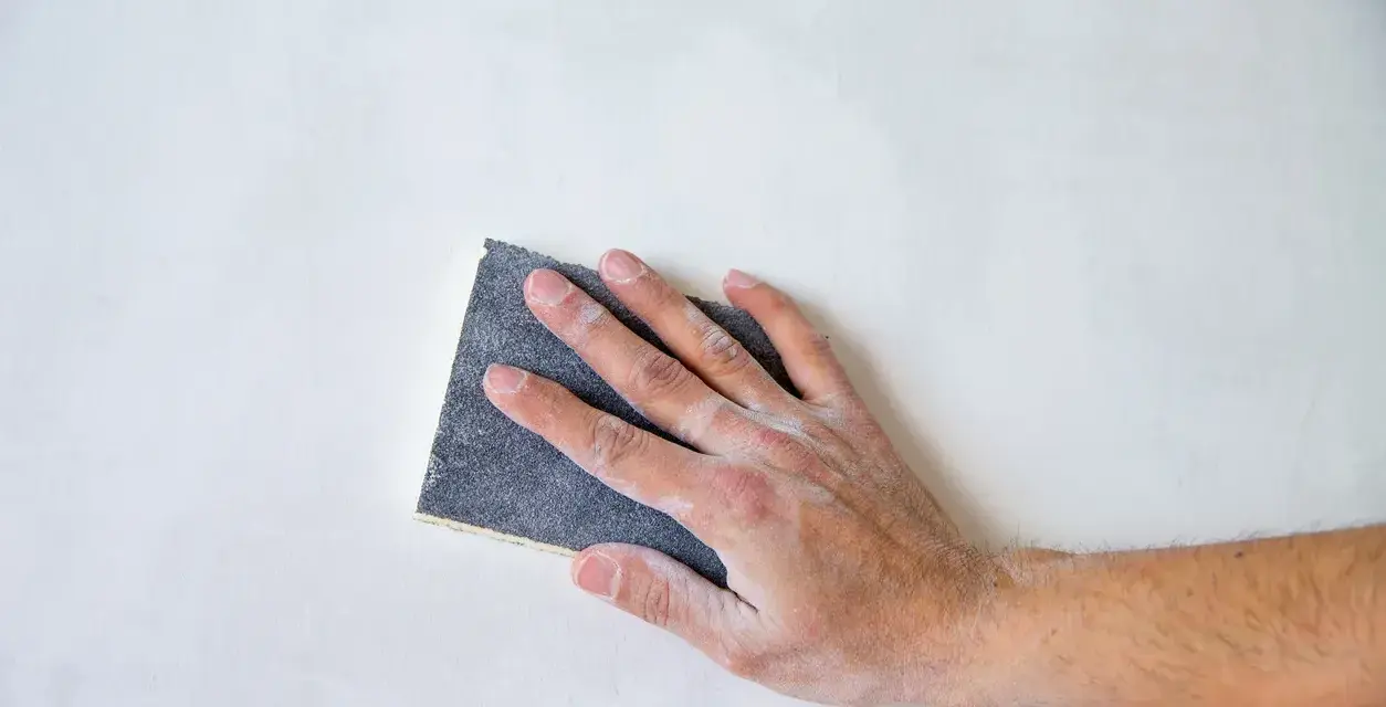 Mano che leviga una superficie bianca con carta vetrata per legno, quale usare per un lavoro perfetto.
