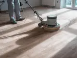 Un professionista usa una levigatrice per decerare il parquet, sollevando una nuvola di polvere.