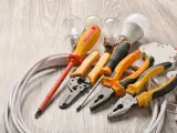 Un set di strumenti per elettricisti: pinze, cacciaviti, lampadine e cavi su un tavolo di legno.