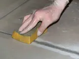 Mano con guanto in lattice che rifinisce le fughe dei pavimenti con una spugna umida.
