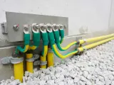 Cavi verdi e gialli collegati a una barra di messa a terra su una parete di cemento, con tubi gialli che escono dal terreno.
