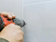 Mani che usano un trapano per fare un buco nel muro bianco.