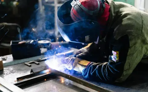Saldatore al lavoro, scintille luminose e fumo blu avvolgono la tempra dell'acciaio inox.